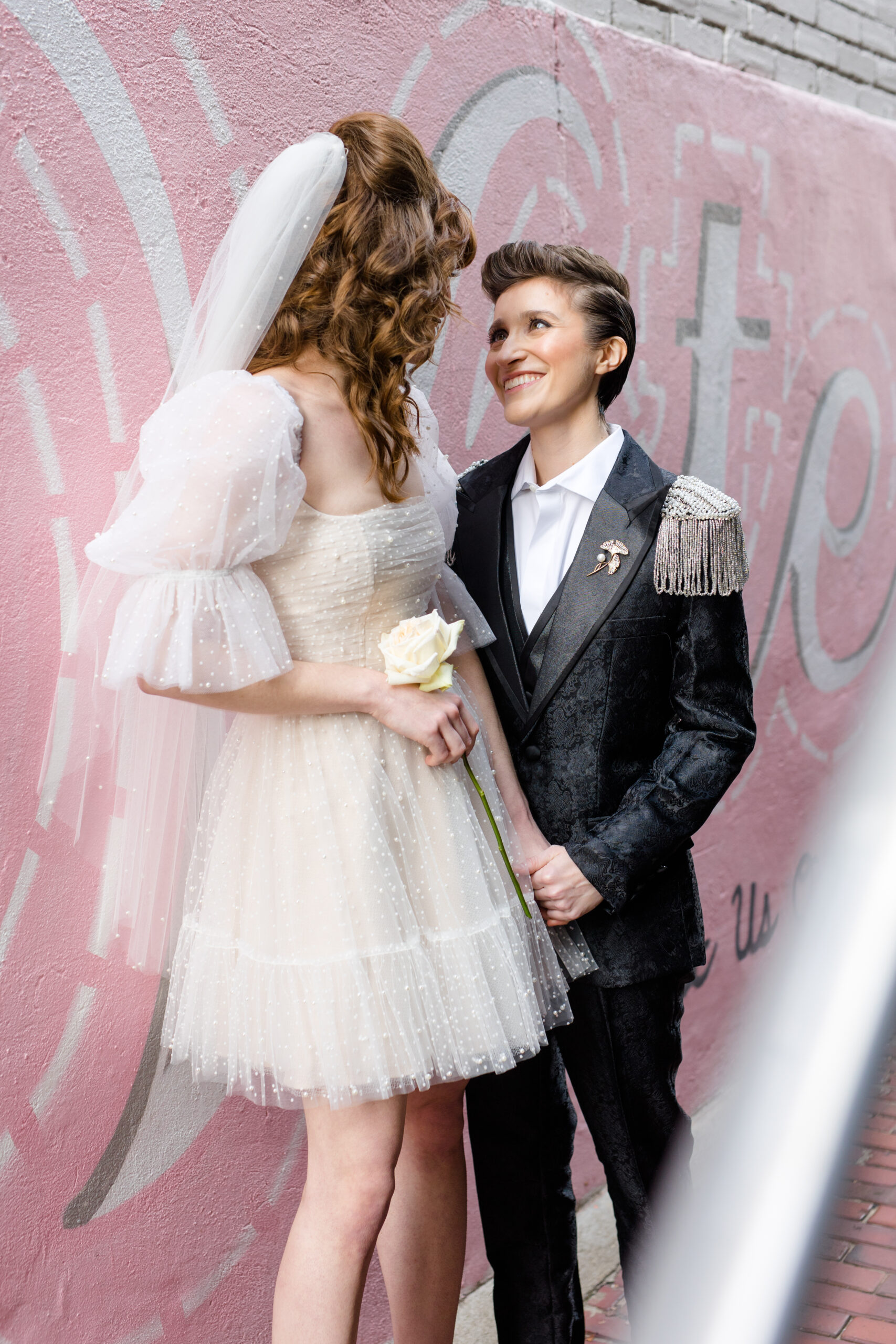 nonbinary wedding couple in white short wedding dress and shiny black pearl suit