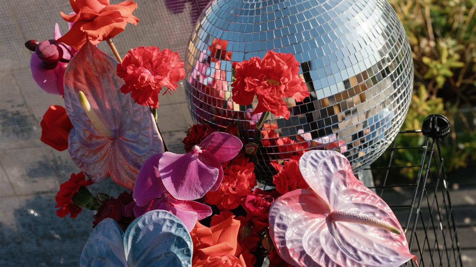 Ceremony altar with column like floral arrangements on black wire crates with vibrant florals of iridescent and rich red & pink hues with a disco ball and against a disco wall backdrop on the terrace at the Line Hotel DC. 