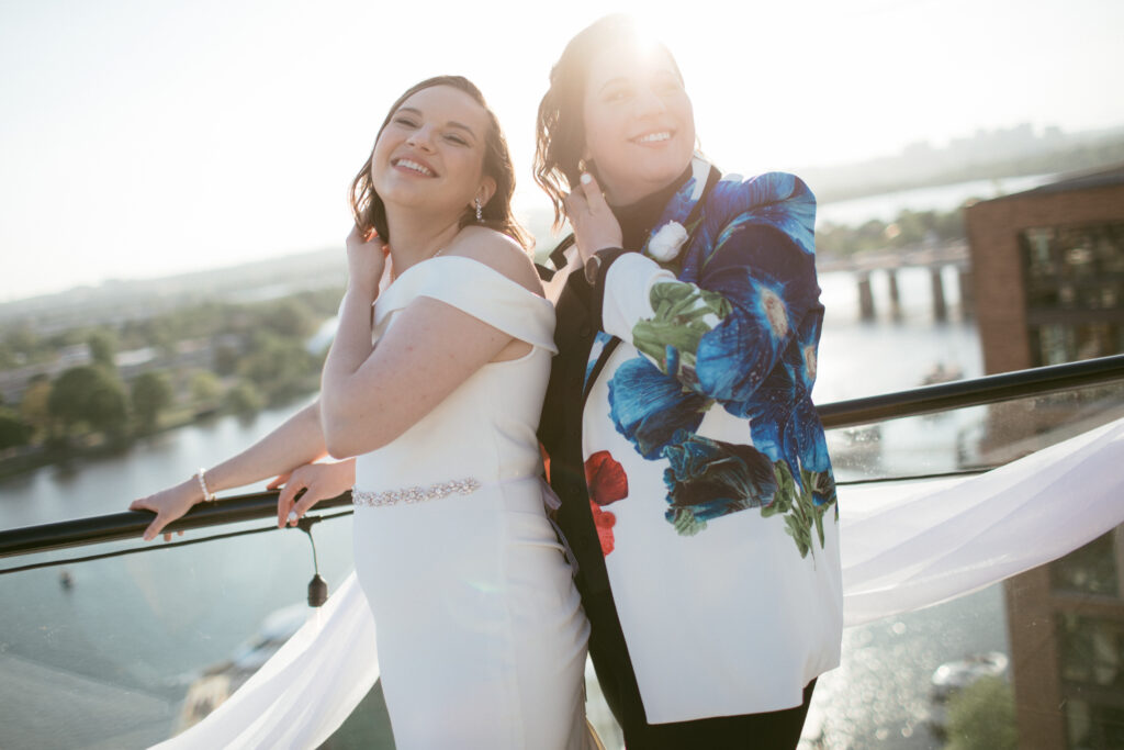 two queer brides holding one another, looking, and smiling off camera on a rooftop terrace at La Vie
